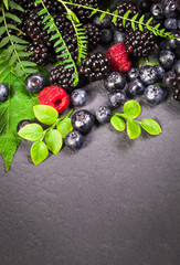 Freshly assorted berries in wooden bowl. Juicy and fresh blueberries6 blackberries and raspberries with green leaves on rustic background. Concept for healthy eating and nutrition.