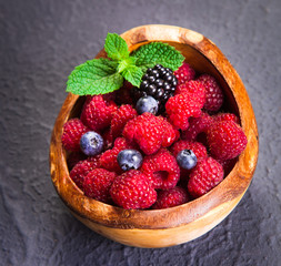 Freshly assorted berries in wooden bowl. Juicy and fresh blueberries6 blackberries and raspberries with green leaves on rustic background. Concept for healthy eating and nutrition.