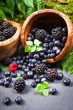 Freshly assorted berries in wooden bowl. Juicy and fresh blueberries6 blackberries and raspberries with green leaves on rustic background. Concept for healthy eating and nutrition.