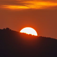 Sun behind mountain at sunrise, orange colors