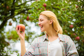 Girl rustic style gather harvest garden autumn day. Farmer pretty blonde with appetite red apple. Woman hold apple garden background. Farm produce organic natural product. Local crops concept