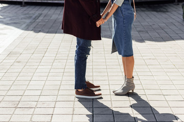 cropped image of couple in autumn outfit holding hands on street in city