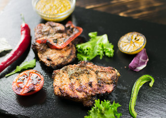 Grilled meat served with vegetables, spices on a slate plate.