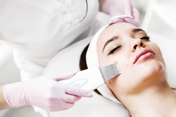 Fototapeta na wymiar The cosmetologist in pink gloves makes the procedure Microdermabrasion of the facial skin of a beautiful, young woman in a beauty salon.Cosmetology and professional skin care. Skin Care.