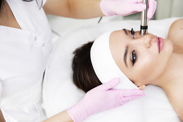 Obraz na płótnie Canvas A woman came to laser hair removal facial. The woman lies and smiles, the doctor leads him in the face with a modern laser epilator. They are in the modern clinic.close up