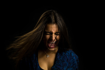 young brunette girl with long straight hair screaming angry, black background