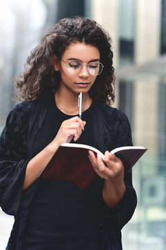 Portrait of a smiling mixed race woman making notes in a notepad while standing outdoors.