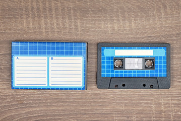 Retro audio cassette and blue case with striped paper to write text. Brown wooden background. - 224334729