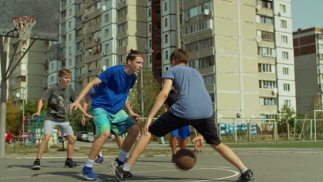 Teenage streetball player dribbling and bouncing the ball on the floor, passing to his teammate while playing basketball game on street. Basketball guard stealing a ball and running in fast break.