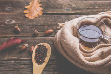 Autumn composition, glass cup of tea and a warm scarf on wooden table background.