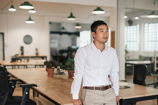 Young Asian Businessman Standing In An Office Deep In Thought