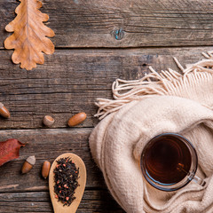 Autumn composition, glass cup of tea and a warm scarf on wooden table background.