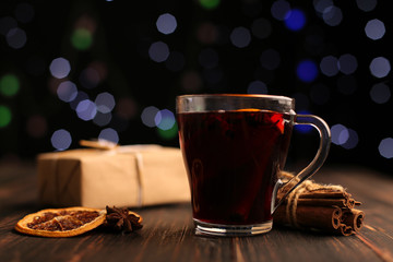 Mulled wine, gift and spices on the background of Christmas lights. On the table next to the tree.