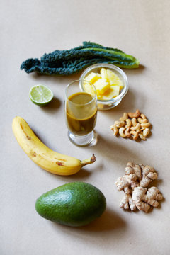 Above view of avocado banana binger pineapple and kale ingredients over a textured brown flat lay background in studio