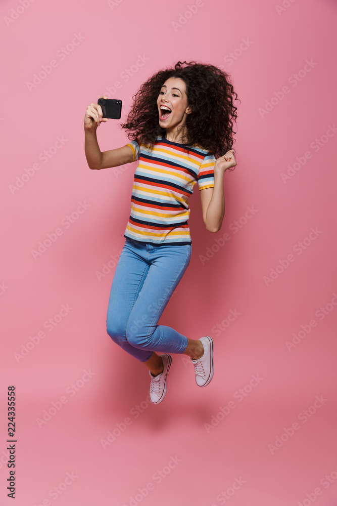 Wall mural full length photo of attractive woman 20s with curly hair holding smartphone and taking selfie photo