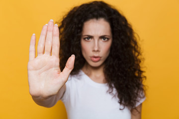 Image of outraged woman 20s with curly hair doing stop gesture with hand, isolated over yellow background