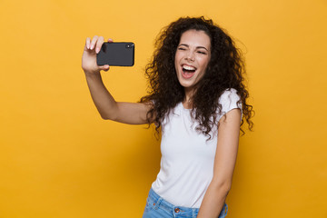 Happy cute young woman posing isolated over yellow background take a selfie by mobile phone.