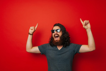 Amazed bearded man pointing up at copy space over red background