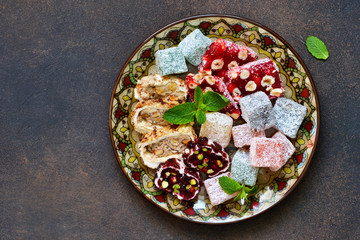 National Turkish dessert. Plate with various pieces of turkish delight lokum on a dark concrete background.