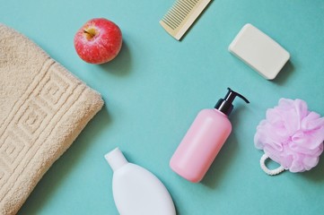 Flat lay beauty mockup/ Beige terry towel, red apple, shampoo package, shower gel, soap bar, wooden comb and pink sponge on a light background. Top view bathroom stuff