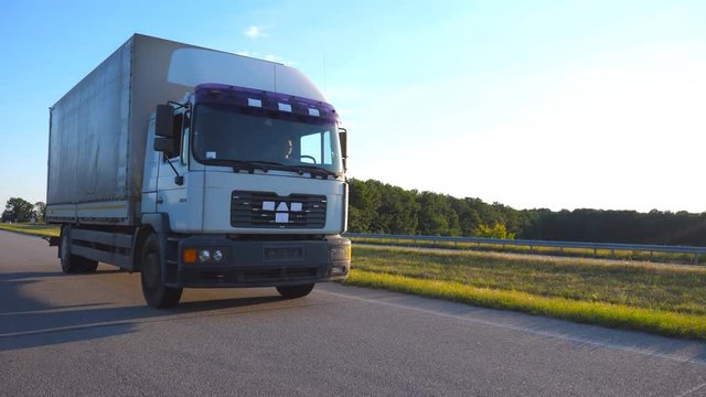 Camera follows to truck driving on a highway. Lorry rides through the countryside with beautiful landscape at background. Front view Slow motion Close up