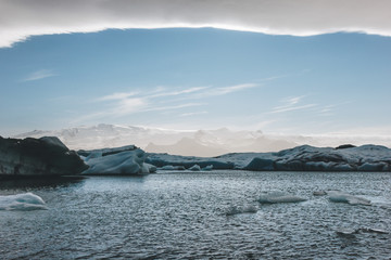 Fototapeta na wymiar glacier ice pieces floating in lake in Jokulsarlon, Iceland under blue sky with mountains on background