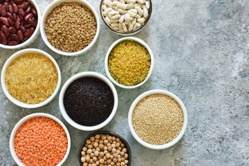 Variation of cereals in bowls: beans, rice, chickpeas, peas on a concrete background.