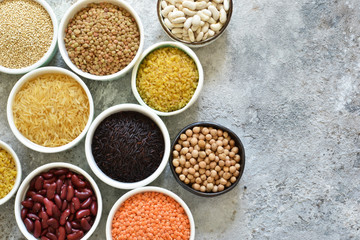 Variation of cereals in bowls: beans, rice, chickpeas, peas on a concrete background.