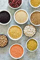 Variation of cereals in bowls: beans, rice, chickpeas, peas on a concrete background.