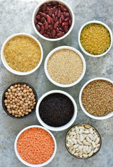 Variation of cereals in bowls: beans, rice, chickpeas, peas on a concrete background.