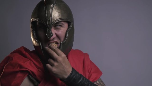 Unshaven legionnaire in helmet looking to the side and eating cookies, bit slow motion