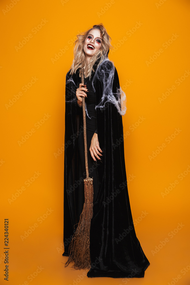 Poster full length image of dangerous witch woman wearing black costume and halloween makeup holding broom,