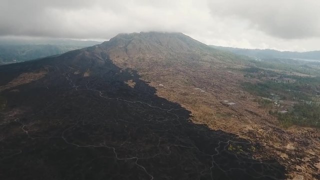Mountain landscape with volcano, traces of lava on the ground, sky with clouds. Aerial view of Mount Batur Volcano in Kintamani. Bali volcano, also referred to as Kintamani is popular sightseeing