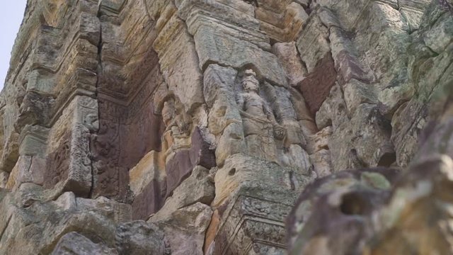 Pan around a female sculpture (devata) on an ancient Khmer temple; low angle; ancient sculptures.