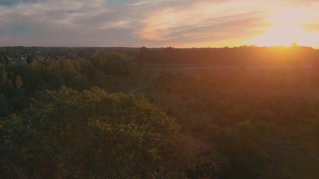 Slow aerial flight circeling over a tree outside nepean city, ontario at sunset with the sun shining over the hill and trees with highway in the background