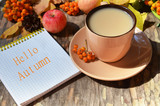 Tag with words hello autumn on the notebook cup of coffee lying on the books with dry yellow maple leaves and everlasting flowers on background