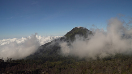 Tops of mountains with running clouds. Landscape slopes of the mountains with the forest in the morning fog and clouds. Banyuwangi Regency of East Java, Indonesia.