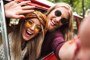 Photo of happy hippie travelers man and woman smiling, and sitting in retro minivan in forest