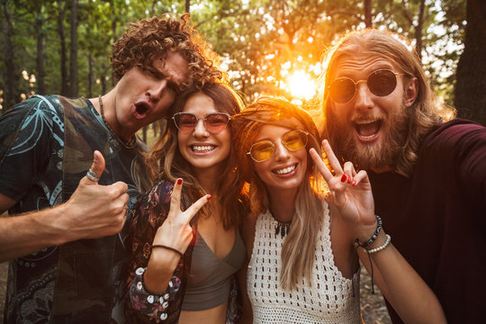 Photo of happy hippie people men and women, smiling and taking selfie in forest