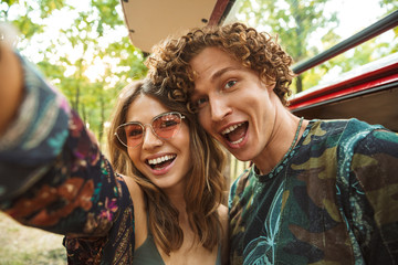 Photo of european hippie couple man and woman smiling, and taking selfie in forest near retro...