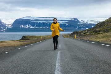 young woman running by empty road in iceland with beautiful mountains and lake on background