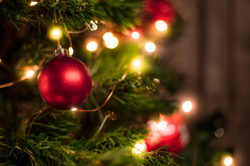 Red Christmas ball on a Christmas tree with a garland on the background of a wooden wall