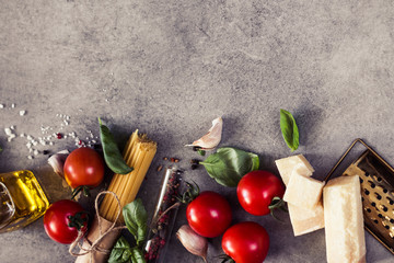 Raw Pasta ingredients. Cherry-tomatoes, spaghetti pasta, garlic, basil, parmesan and spices on dark grunge backdrop, copy space, top view