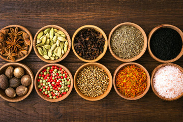 Spices on a wooden background in bowls, place of copying, seasoning, saffron, cumin, black sesame, cardamom, nutmeg, pink salt, star anise, coriander
