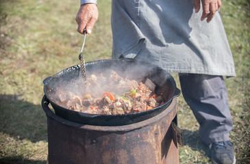 Man cooking meat and vegetables in wok outdoors.
