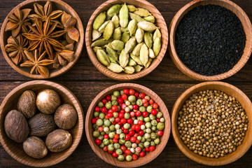 Spices on a wooden background in bowls, place of copying, seasoning, saffron, cumin, black sesame, cardamom, nutmeg, pink salt, star anise, coriander