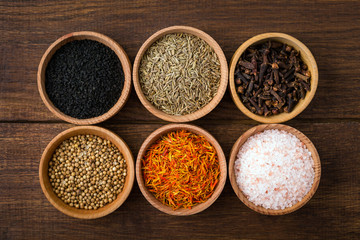 Spices on a wooden background in bowls, place of copying, seasoning, saffron, cumin, black sesame, cardamom, nutmeg, pink salt, star anise, coriander