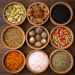 Spices on a wooden background in bowls, place of copying, seasoning, saffron, cumin, black sesame, cardamom, nutmeg, pink salt, star anise, coriander