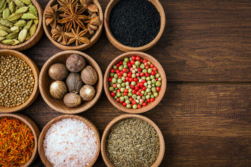 Spices on a wooden background in bowls, frame, place of copying, seasoning, saffron, cumin, black sesame, cardamom, nutmeg, pink salt, star anise, coriander
