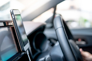 Male driver hand holding on steering wheel using smartphone for GPS navigation. Mobile phone...